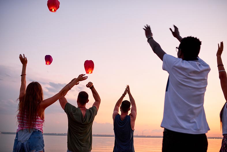 excited young people saying goodbye to flying sky lanterns